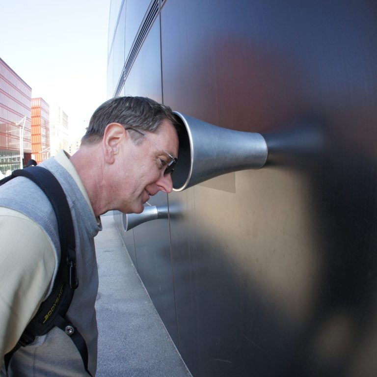 Mann schaut durch ein Rohr an einer Wand, um etwas zu hören oder zu sehen.